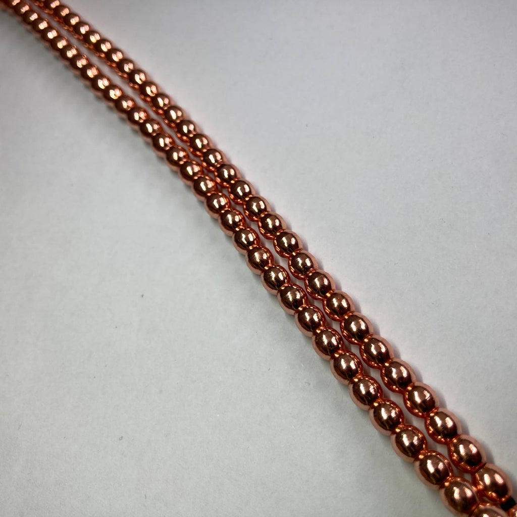 A close-up of a strand of small metallic copper beads arranged diagonally on a plain light gray background.