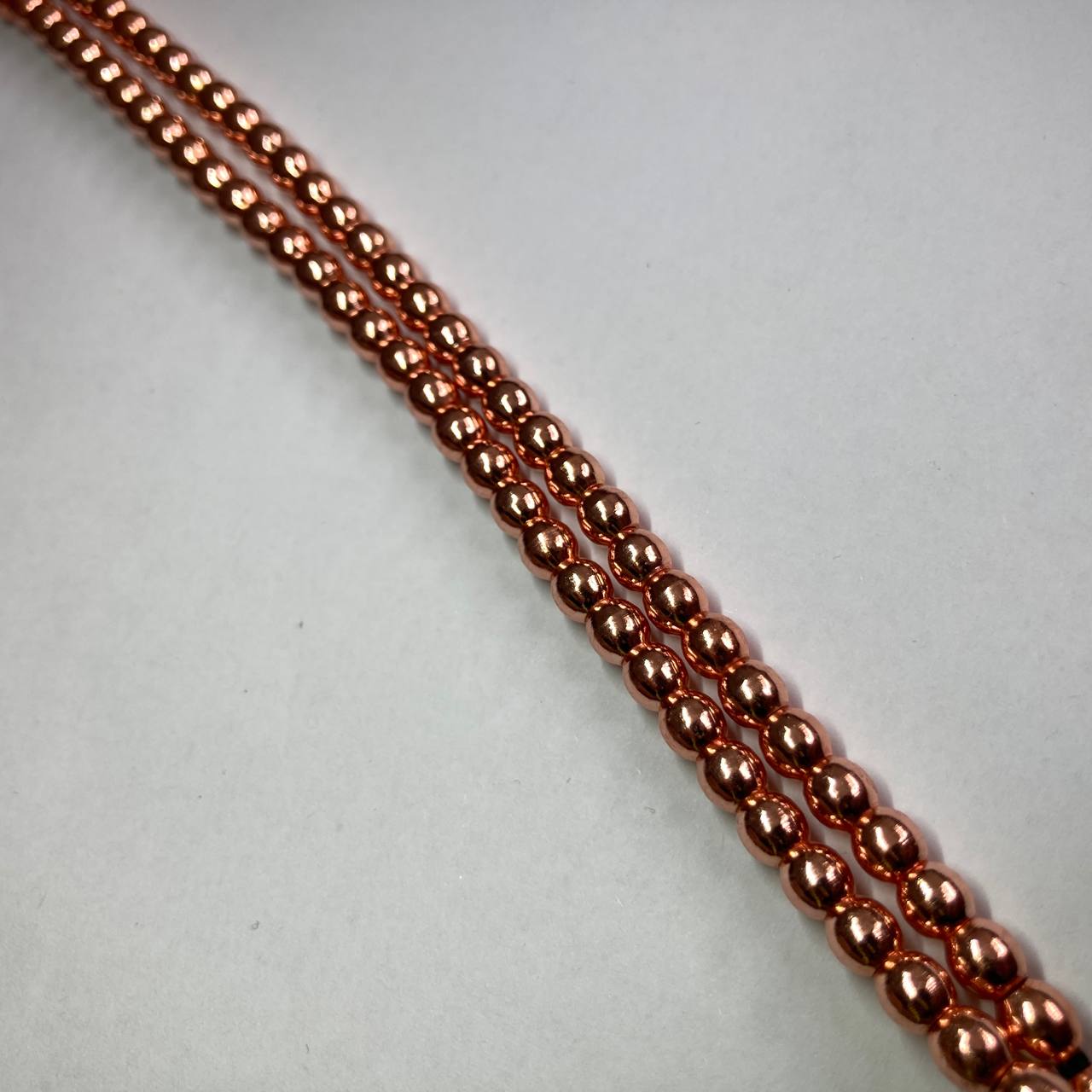 A close-up of a strand of small metallic copper beads arranged diagonally on a plain light gray background.