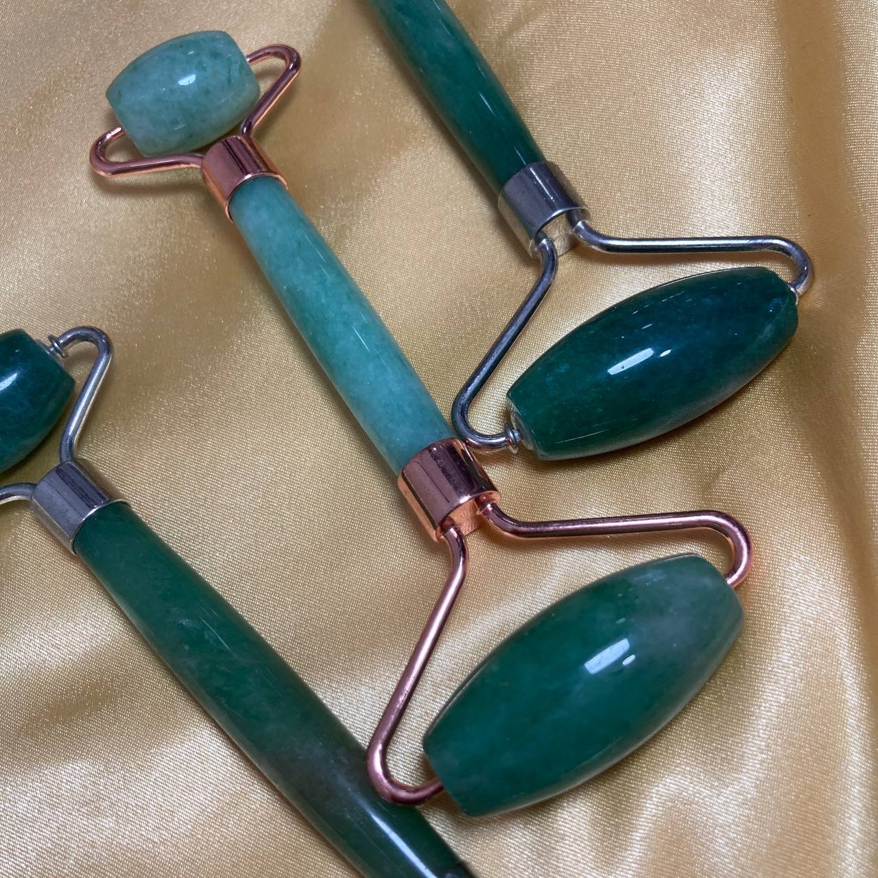 Three green jade rollers on a beige fabric background