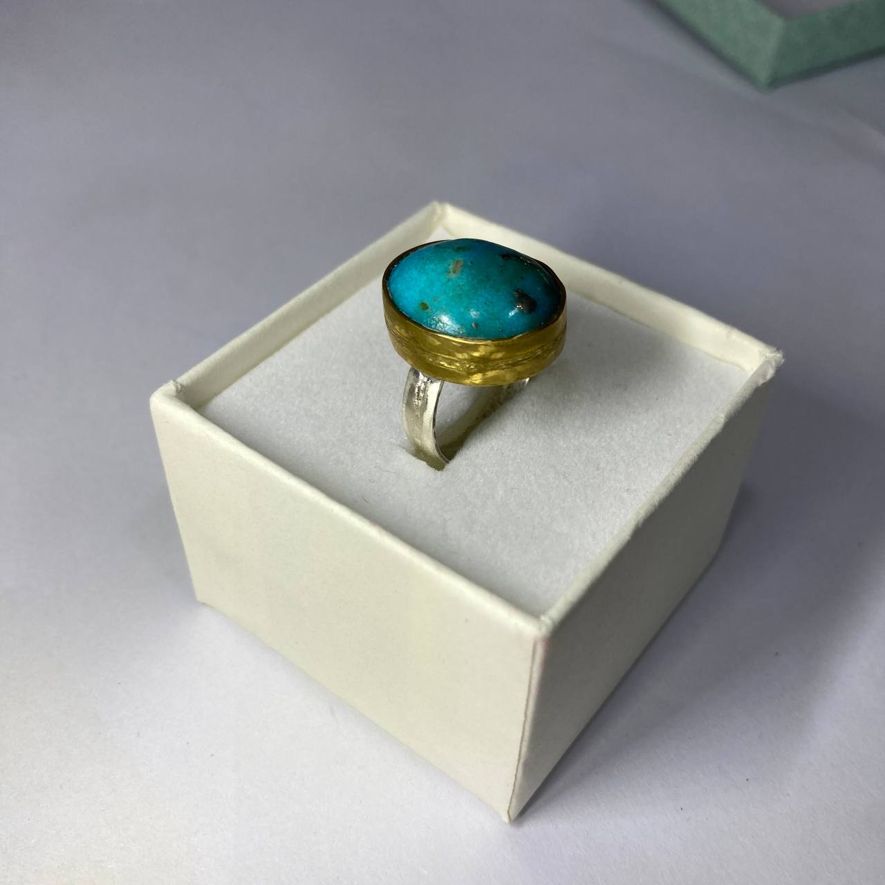 Ring with turquoise stone and brass accents in a box on a white background