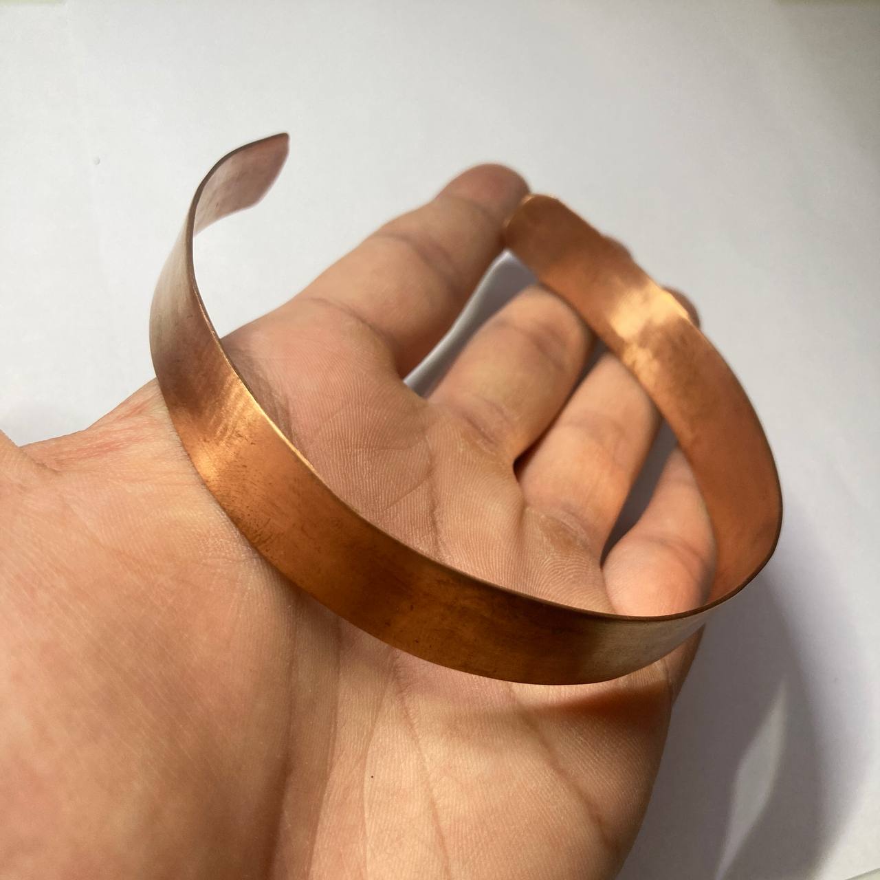 A hammered copper-colored metal cuff bracelet held in a person's hand against a plain light background.