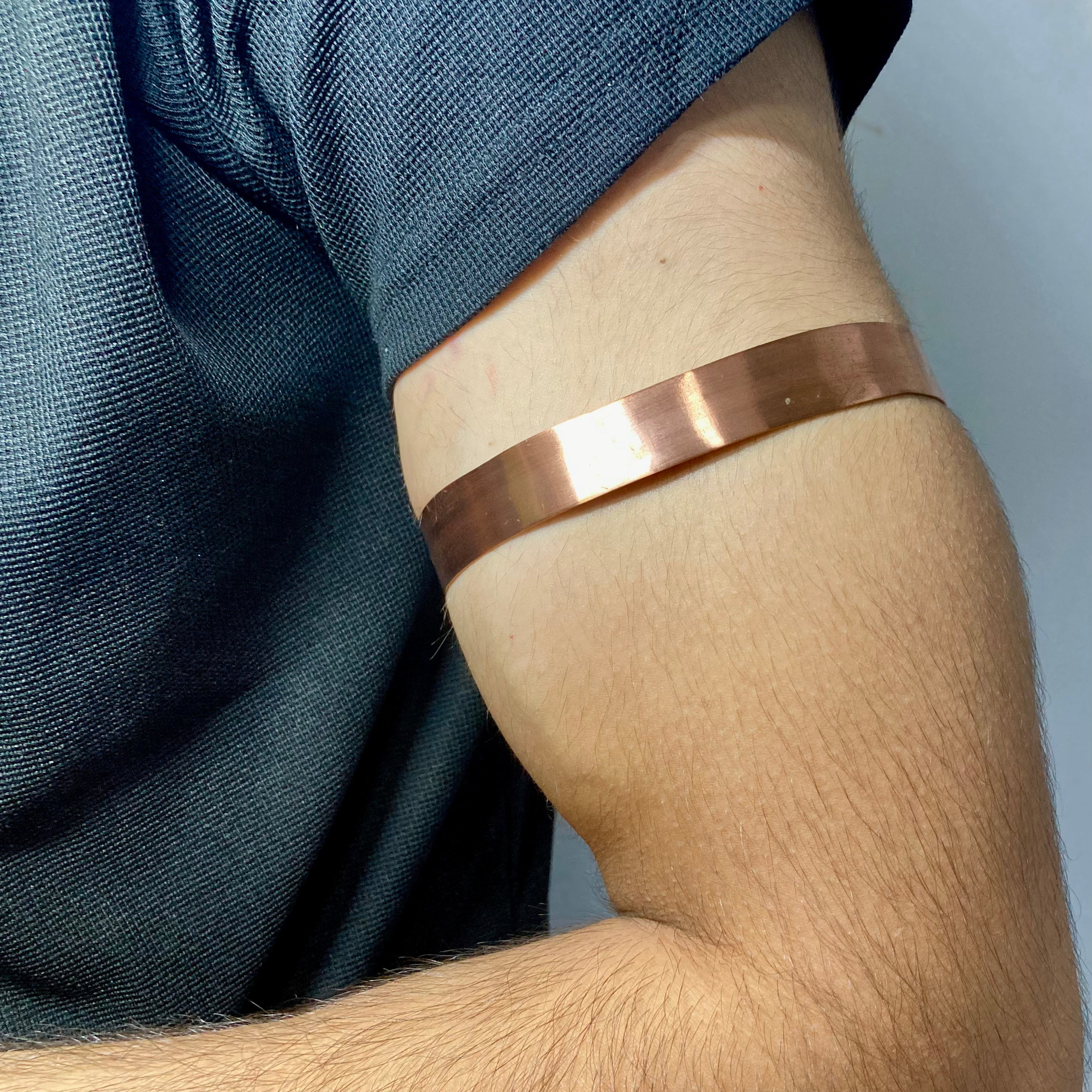 A close-up of a person's upper arm wearing a wide, polished copper-colored metallic bangle or cuff bracelet.