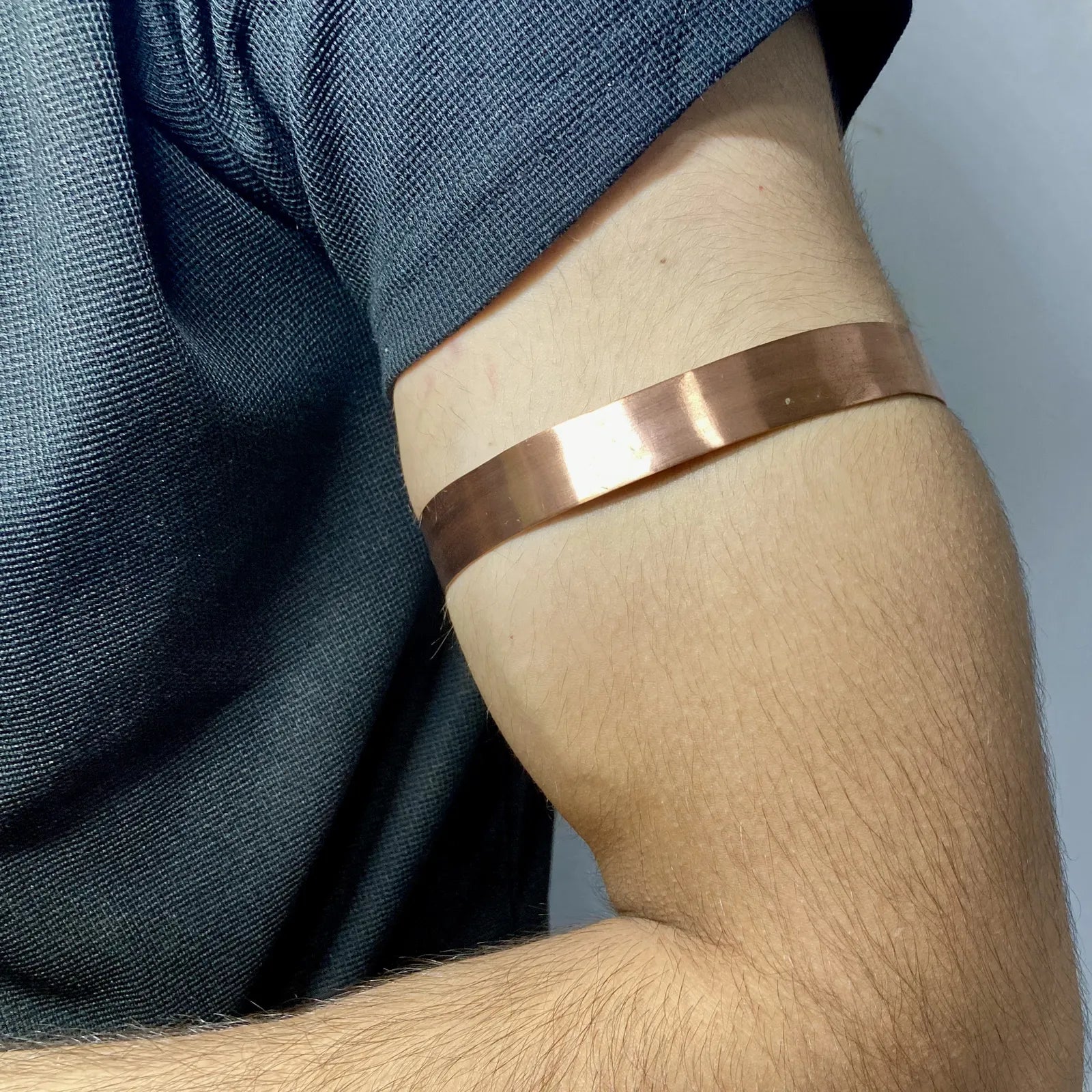 A close-up of a person's upper arm wearing a wide, polished copper-colored metallic bangle or cuff bracelet.