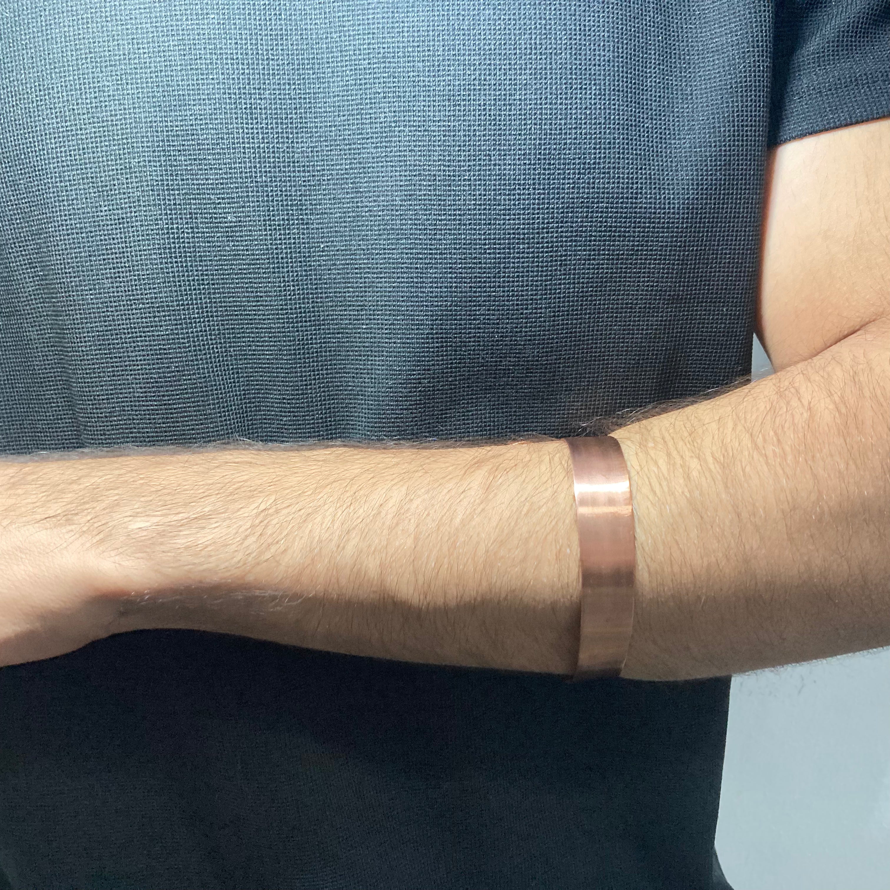 A close-up of a person's forearm wearing a polished copper-colored copper cuff bracelet.