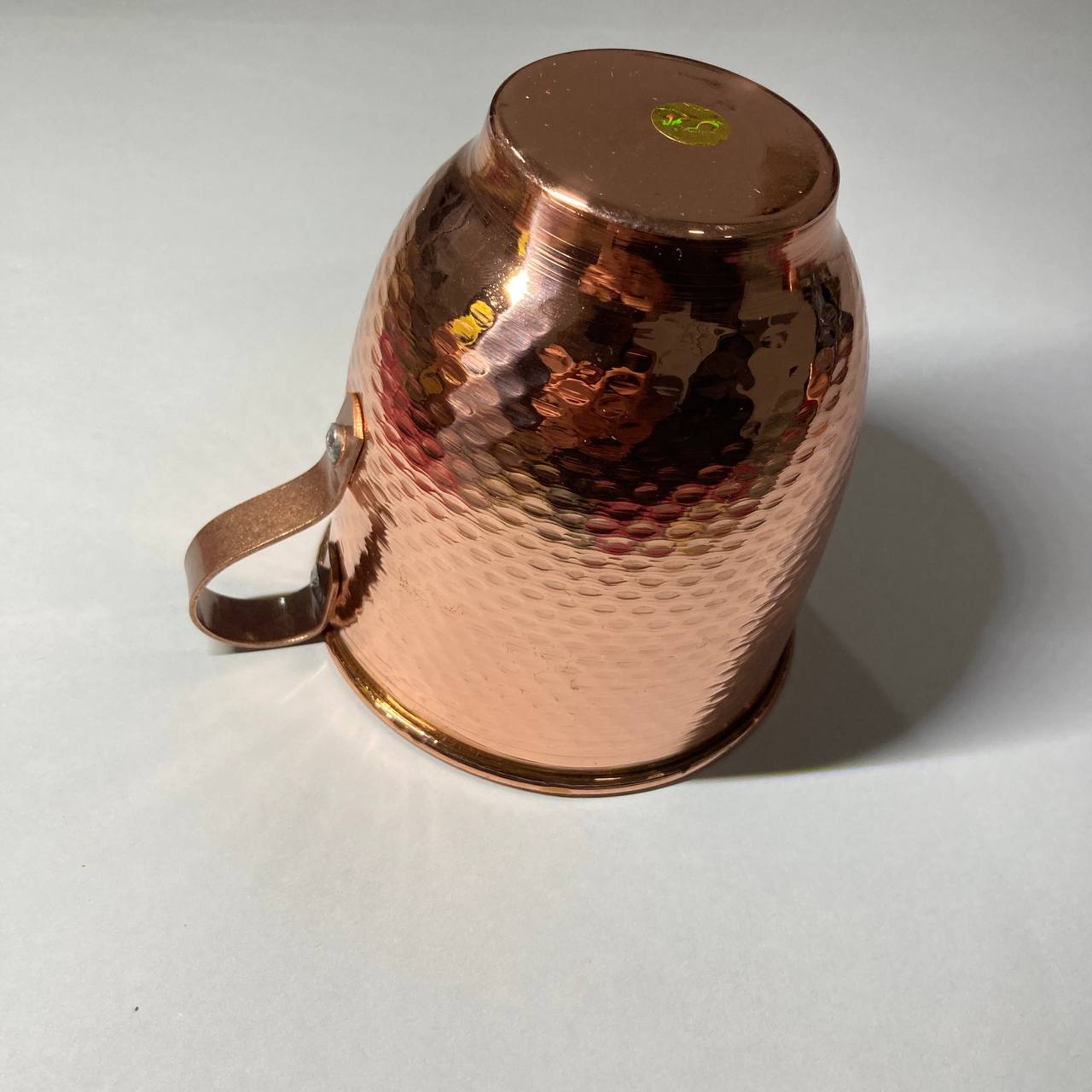 A hammered copper mug with a matching copper handle, photographed on a plain light gray background.