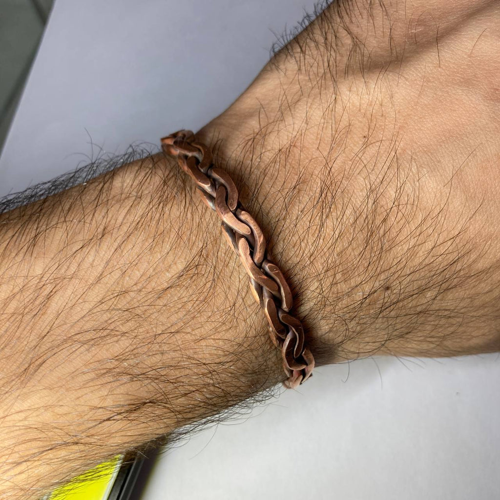 Close-up of a wrist wearing a brown chain bracelet on a neutral background