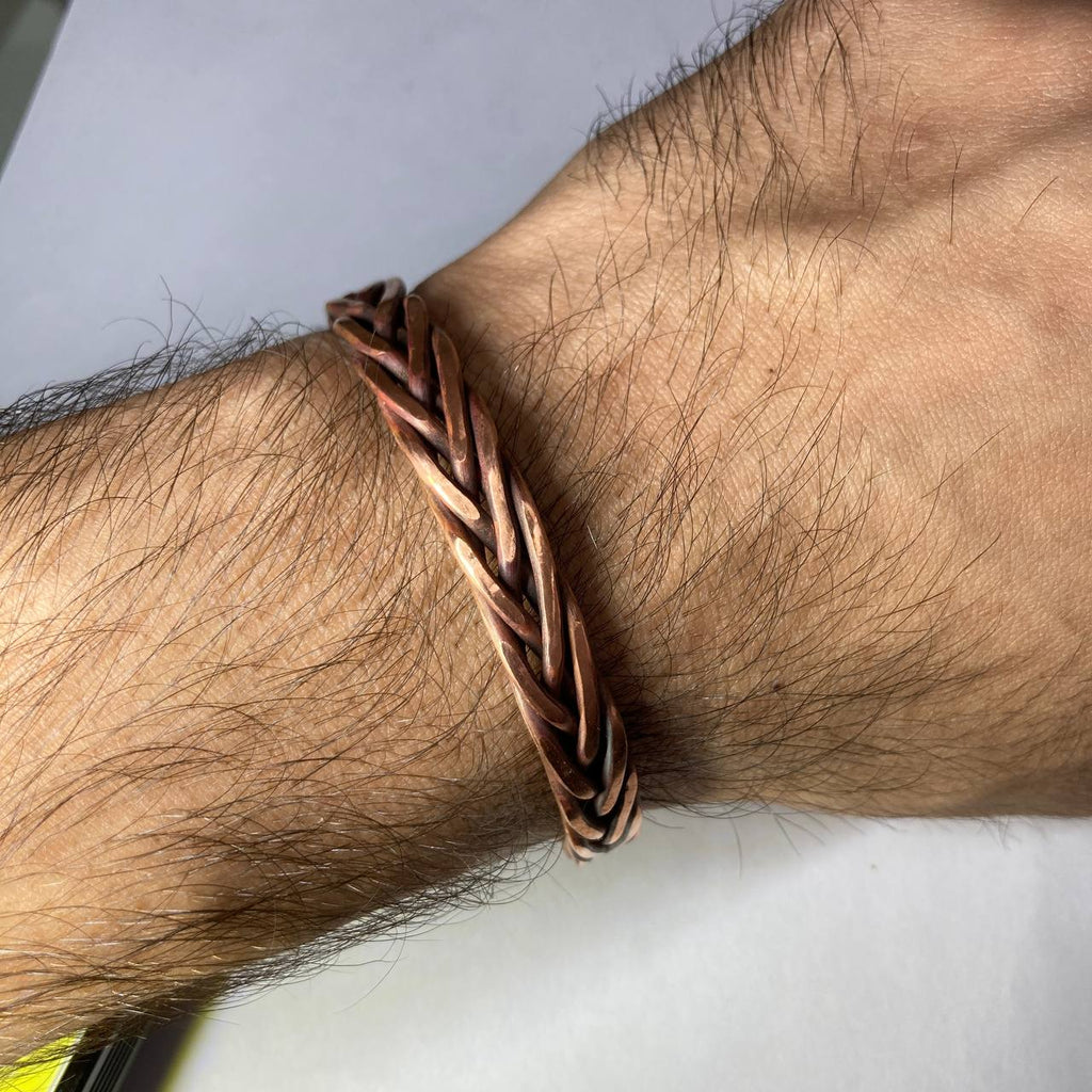 Close-up of a braided copper bracelet on a person's wrist with a neutral background