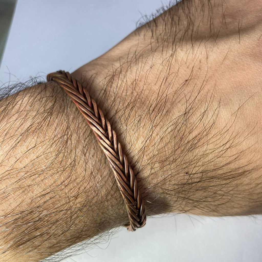 Close-up of a braided copper bracelet on a wrist with a neutral background
