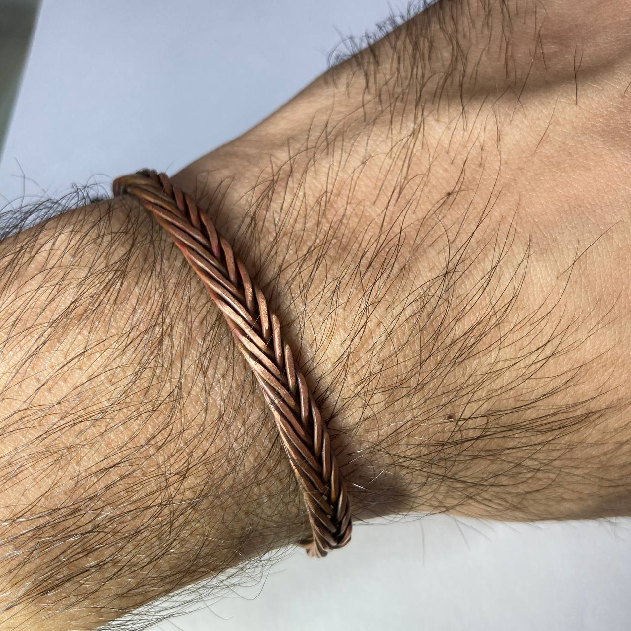 Close-up of a braided copper bracelet on a wrist with a neutral background