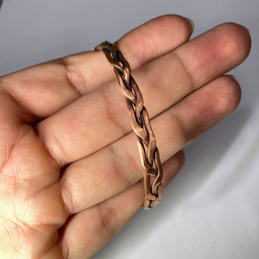 Copper chain bracelet on a hand against a plain background