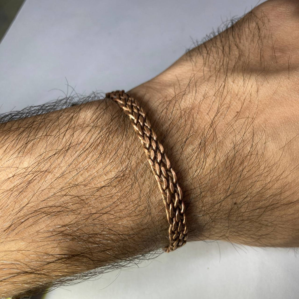 Brass chain bracelet on a wrist with a neutral background